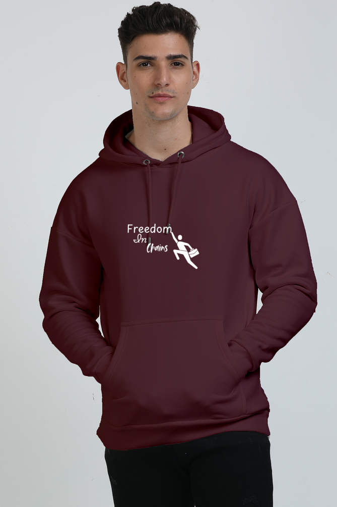 A man wearing a Maroon unisex oversized hoodie with the text 'FREEDOM IN CHAINS' with a man toucing the letter "m"printed on the front.
