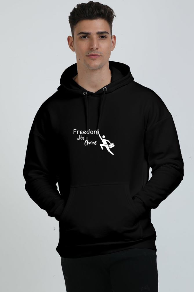 A man wearing a black unisex oversized hoodie with the text 'FREEDOM IN CHAINS' with a man toucing the letter "m"printed on the front.