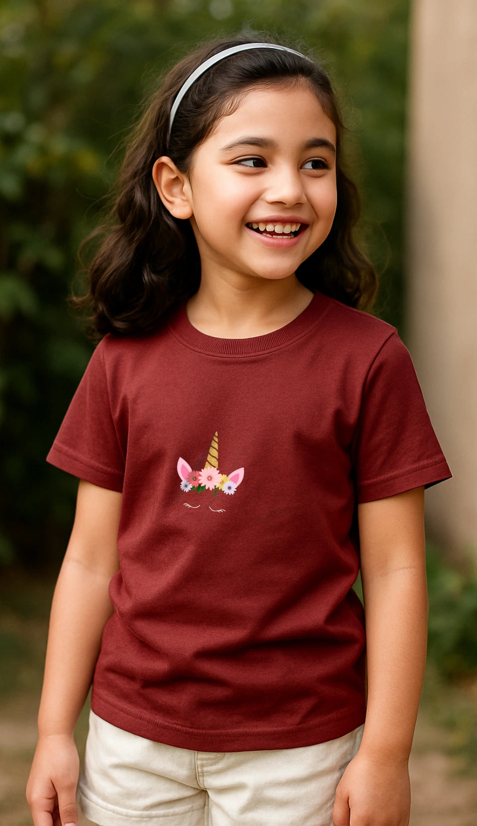 Young girl wearing a maroon t-shirt with a pony crown design outdoors.