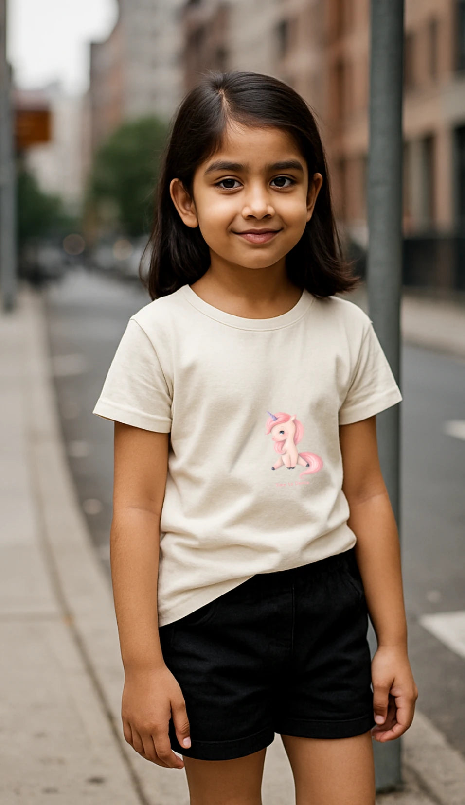 Young girl wearing a white t-shirt with a pony design on pavement in city.