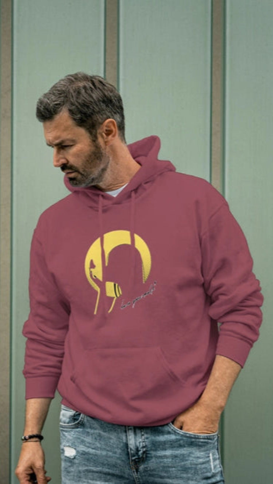 Man wearing a maroon hoodie with a logo against a green wall