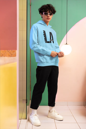 Model in Baby Blue Heavyweight Hoodie. Oversized fit, LA Hollywood graphic, and sunglasses for street fashion.