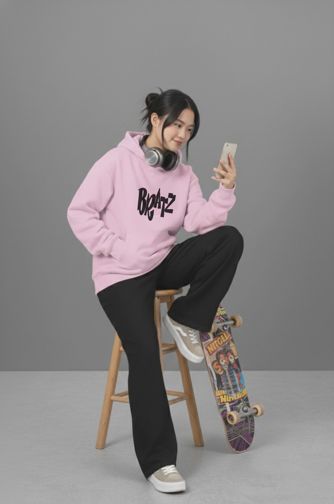 Woman sitting on stool with skateboard in Pink Heavyweight Hoodie. Mischief related graphic in black and relaxed fit.