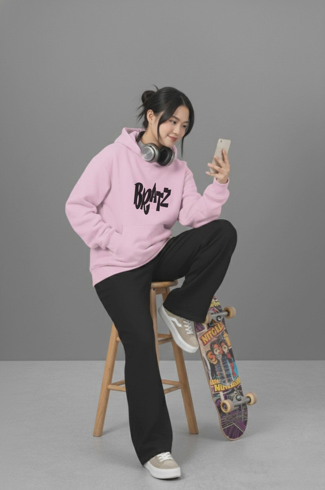 Woman sitting on stool with skateboard in Pink Heavyweight Hoodie. Mischief related graphic in black and relaxed fit.