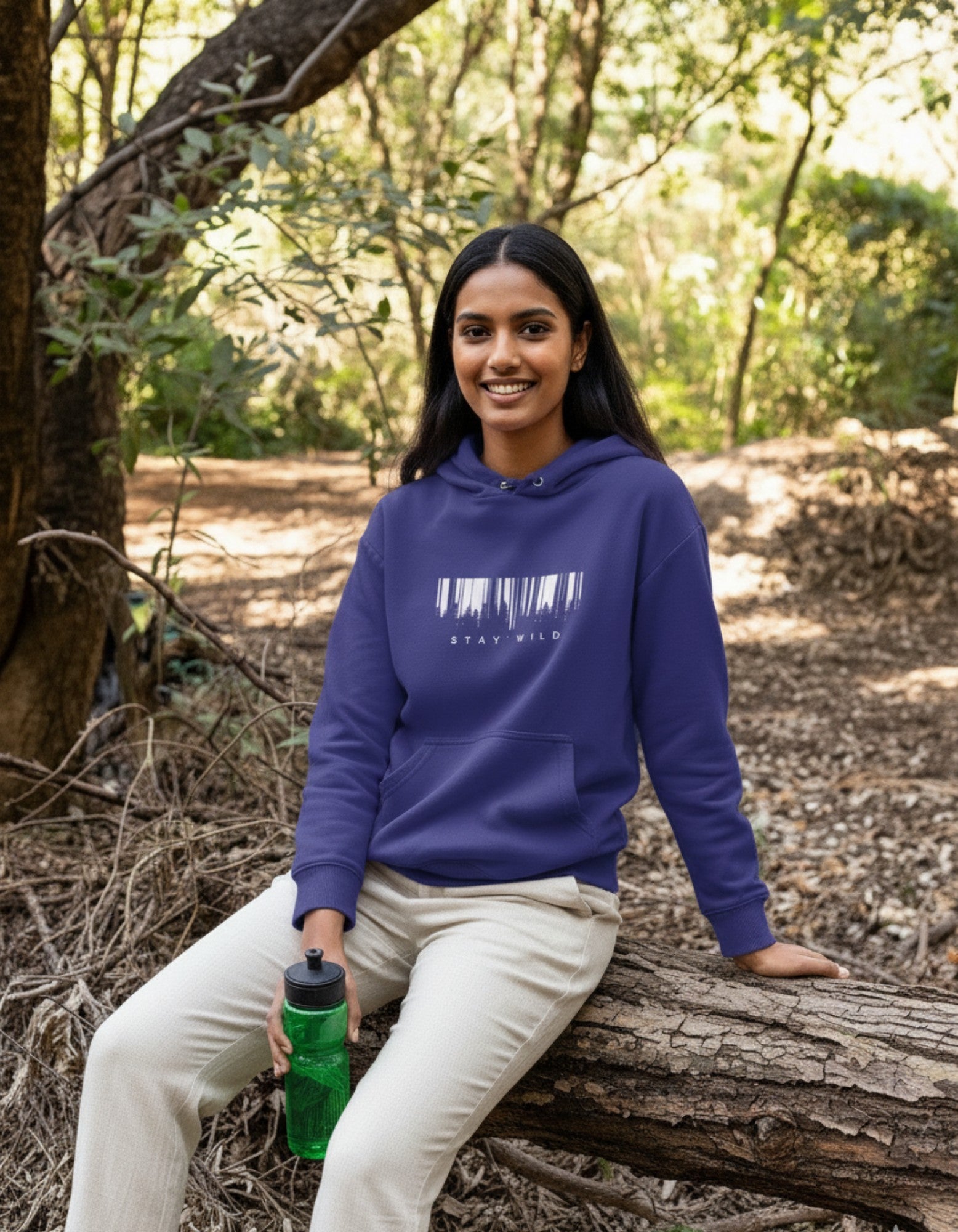 Person wearing a royal blue premium cotton hoodie with a stay wild design, sitting on a log in a forest.