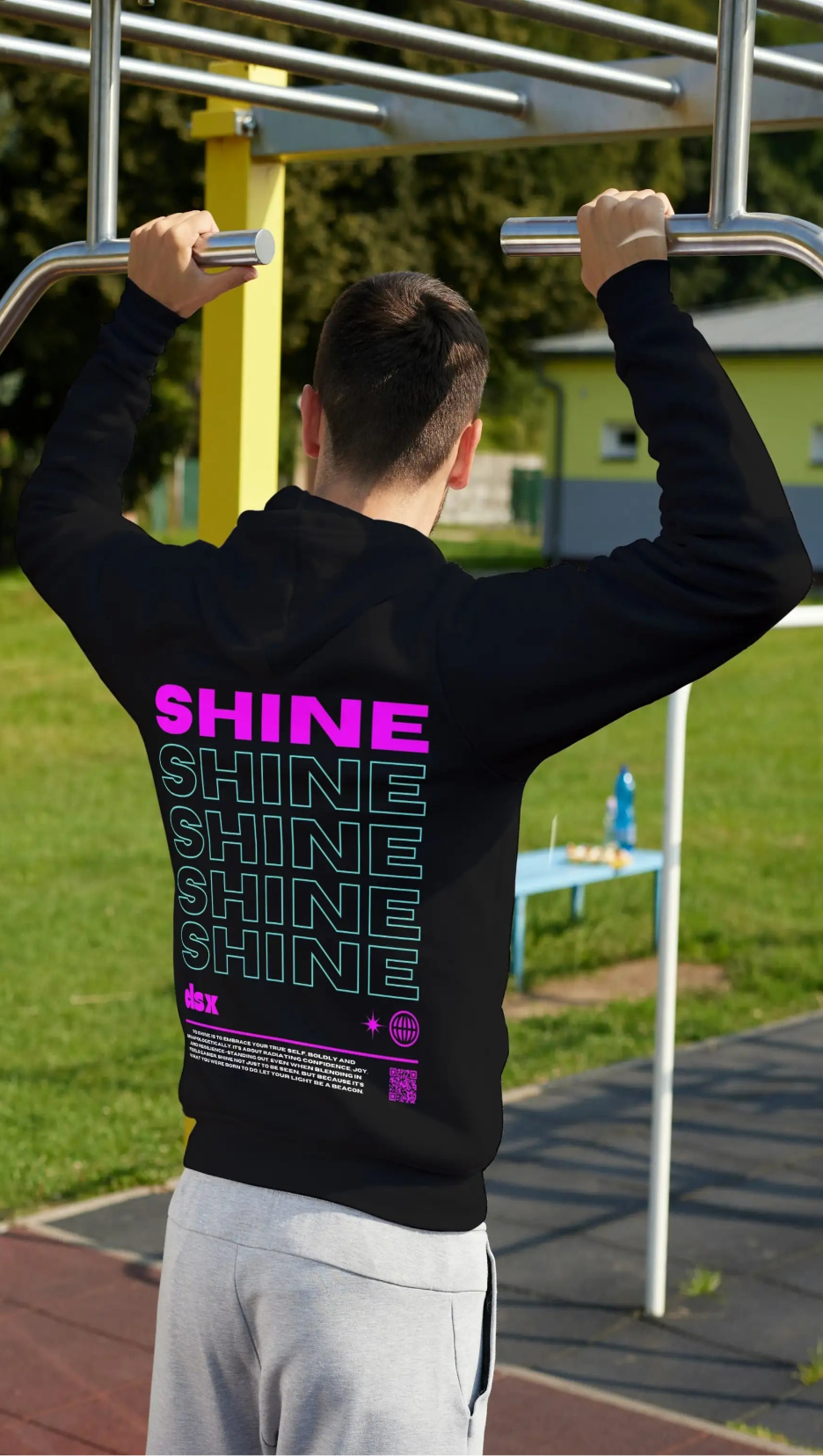 Person wearing a black hoodie with 'SHINE' branding doing pull-ups on outdoor gym equipment.