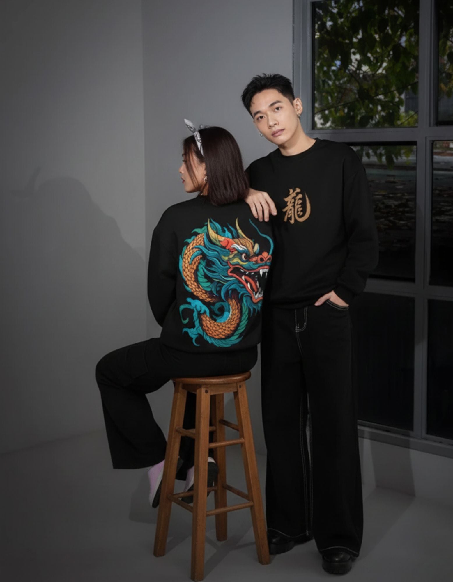 Two people wearing black sweatshirts with dragon designs in a room.