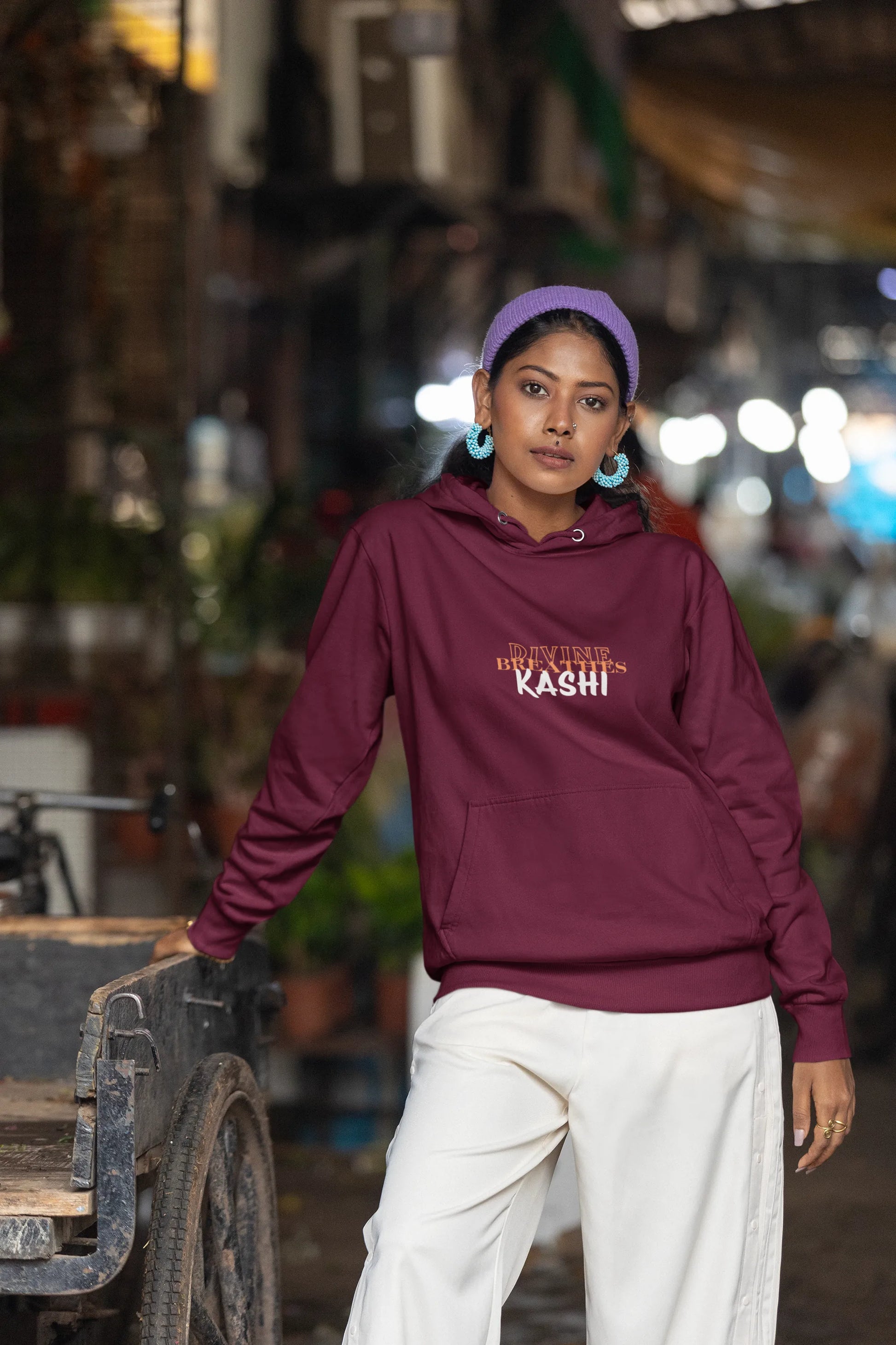 Man wearing aMaroon hoodie with text "DIVINE BREATHE KASHI", standing in an Nursery.