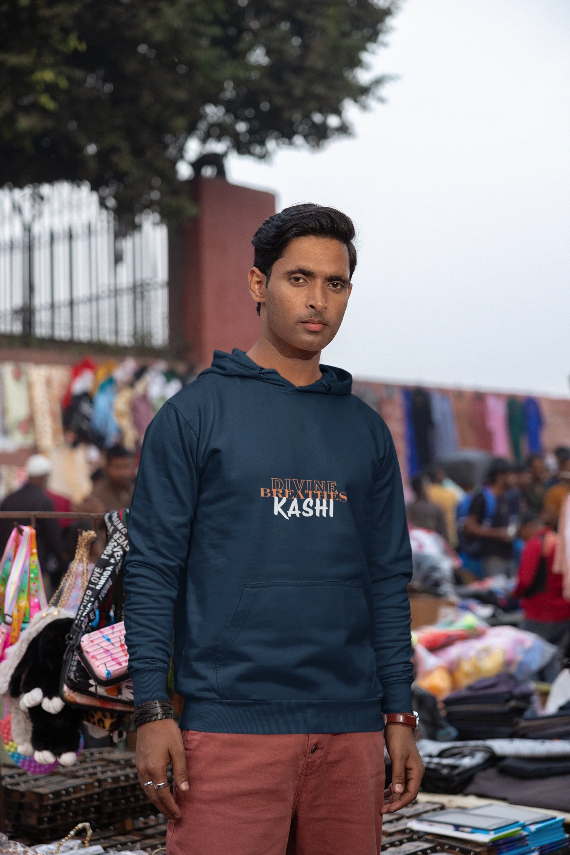 Man wearing a Navy Blue hoodie with text "DIVINE BREATHE KASHI", standing in an Saturday Market.